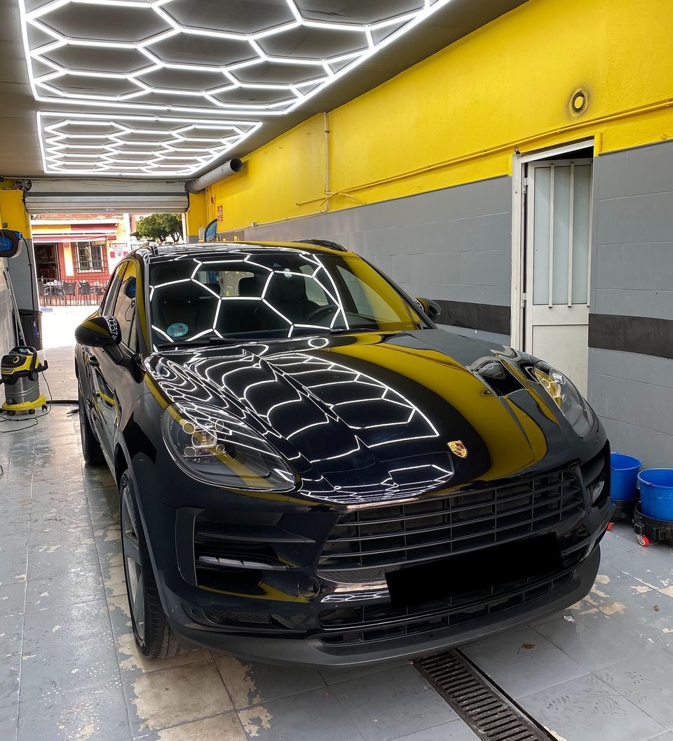 Black Porsche Macan at our car wash in San Pedro de Alcántara, with the hexagonal LED ceiling reflected on the bonnet